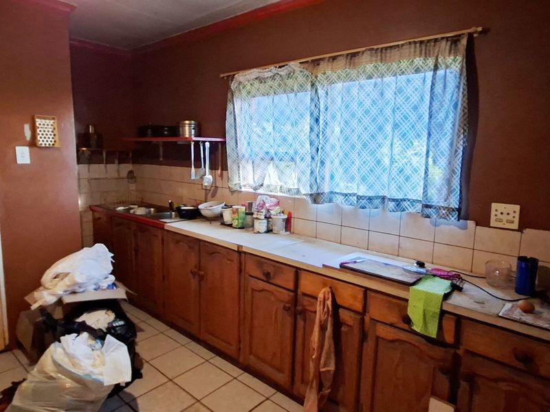 A dated kitchen featuring wooden cabinetry, tiled backsplash, and tiled flooring, offering significant potential for modernization and renovation.