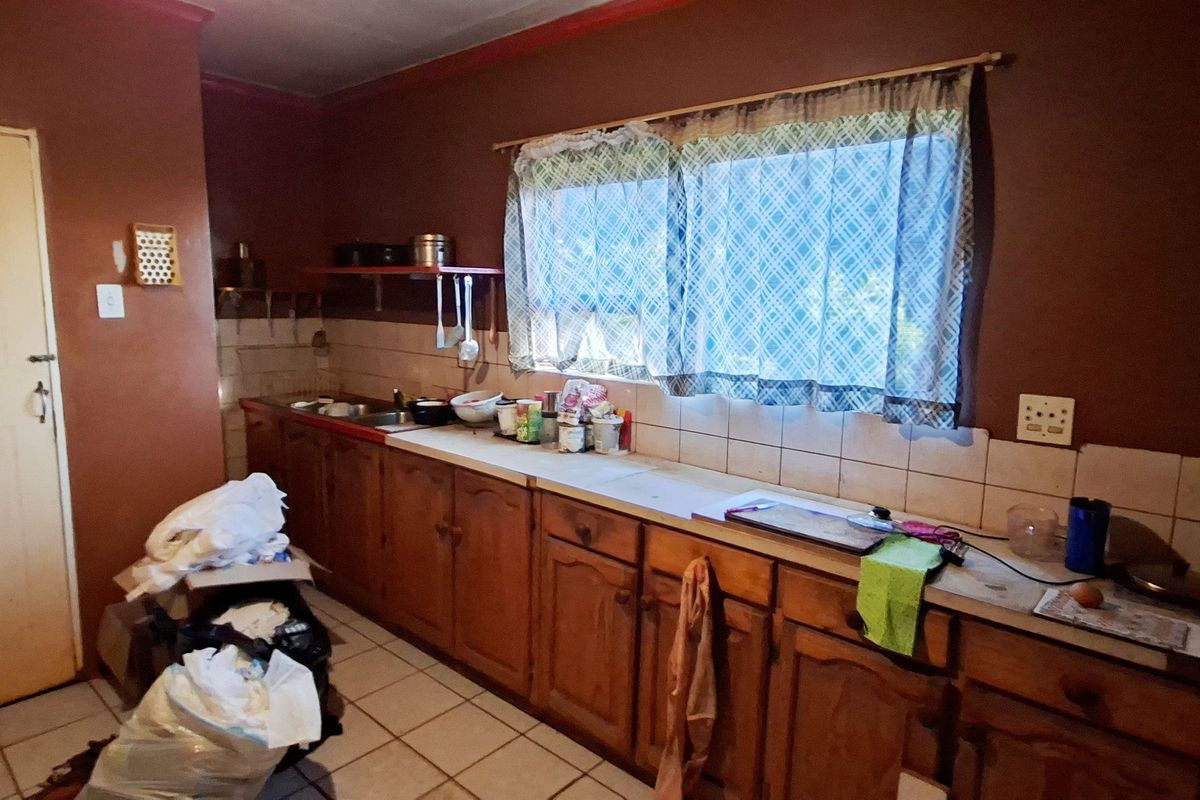 A dated kitchen featuring wooden cabinetry, tiled backsplash, and tiled flooring, offering significant potential for modernization and renovation.