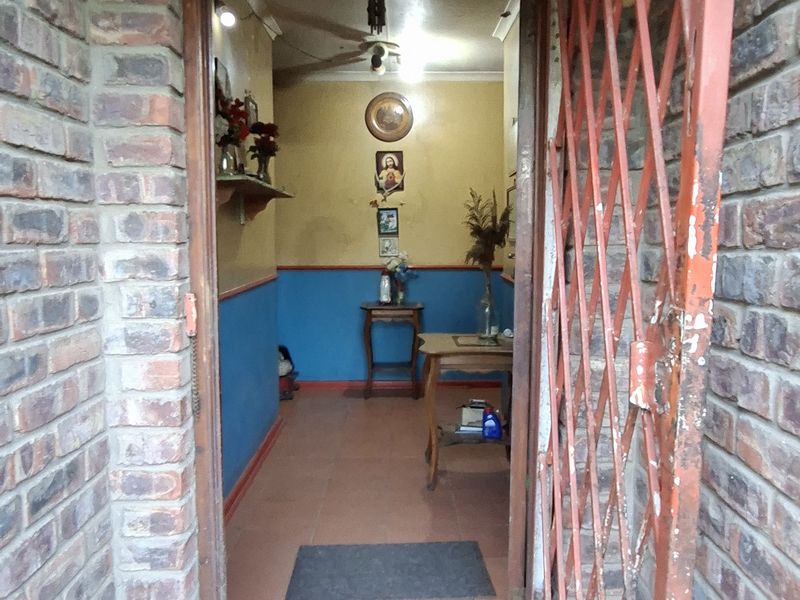 Entrance area featuring exposed brick walls, tiled flooring, and a metal security gate showing signs of wear.