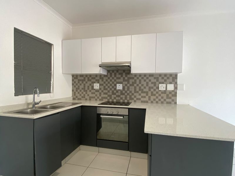 Modern kitchen featuring dark grey lower cabinets, white upper cabinetry, stone countertops, integrated oven, hob, and extractor fan with a tiled backsplash.