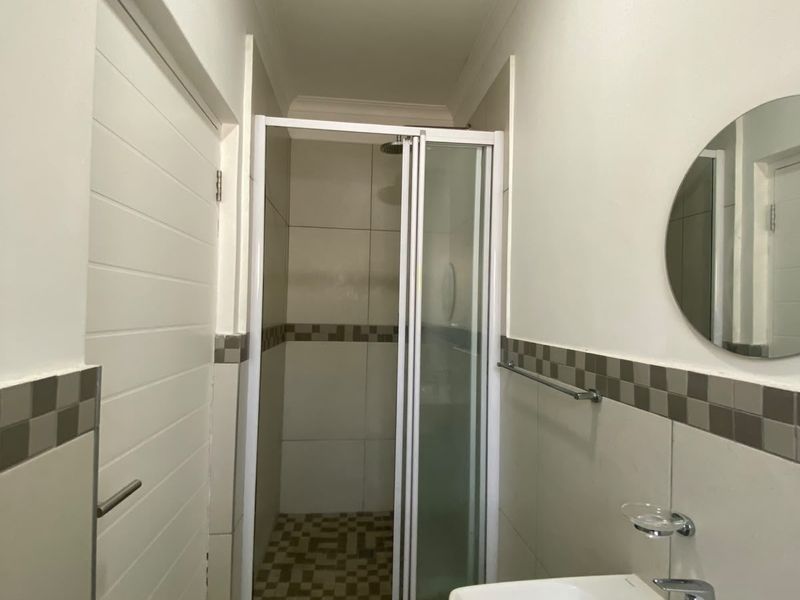 A clean and functional bathroom featuring a shower enclosure, wall-mounted basin with chrome mixer tap, and neutral tiled accents.