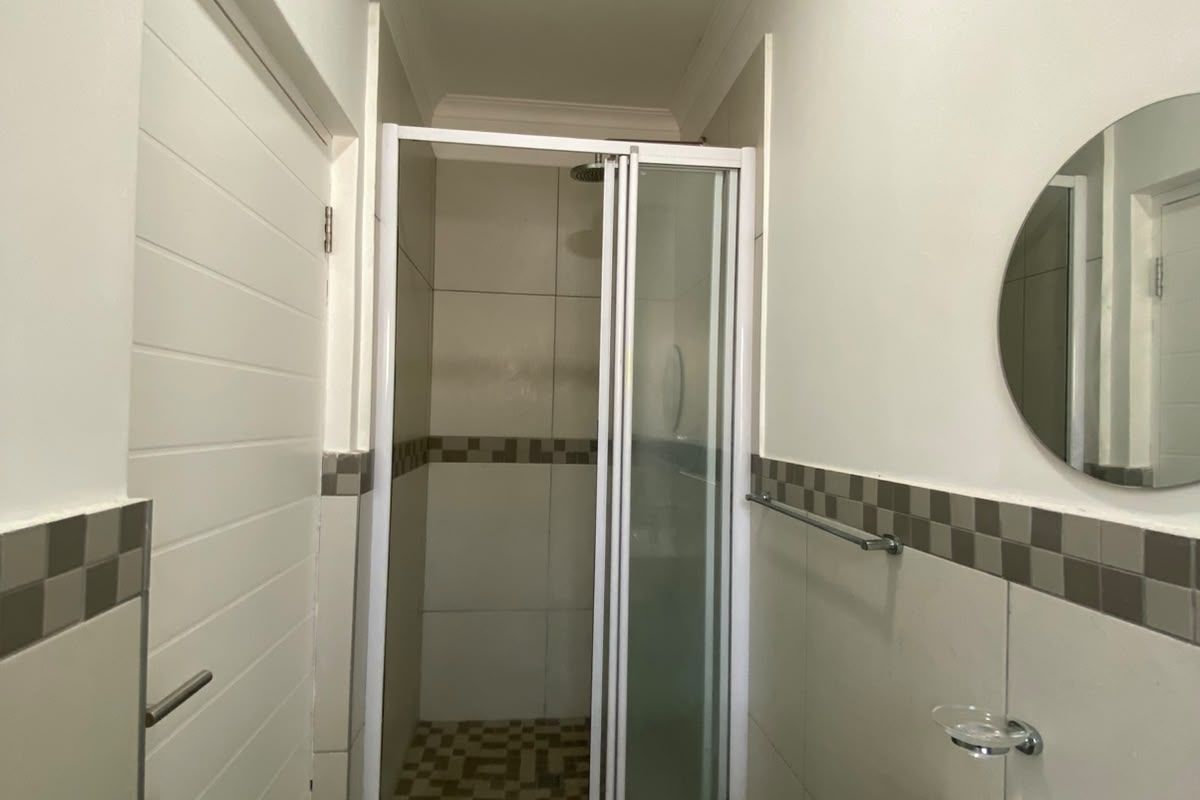 A clean and functional bathroom featuring a shower enclosure, wall-mounted basin with chrome mixer tap, and neutral tiled accents.