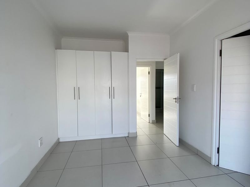 A clean, empty bedroom featuring neutral tiled flooring, white walls, and built-in storage cupboards, offering a blank canvas for personalization.