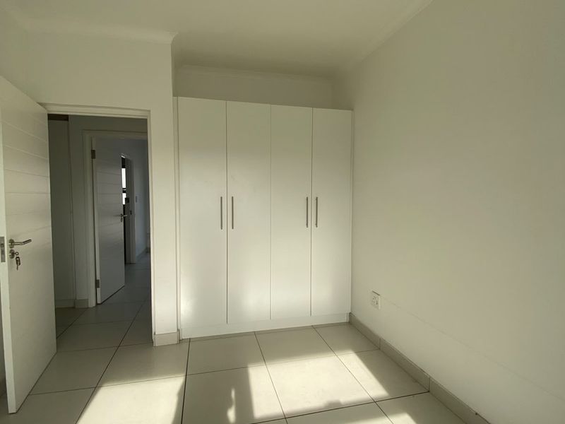 A bright, empty bedroom featuring neutral tiled flooring and white built-in cupboards, offering a clean and versatile space.