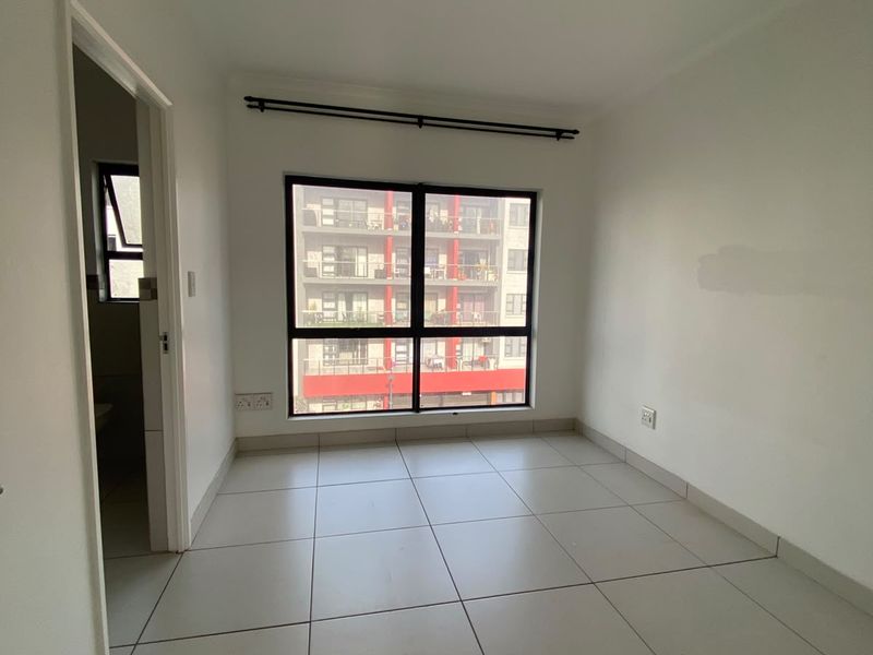 An empty bedroom featuring neutral tiled flooring, a large window with a curtain rod, and access to an adjacent bathroom.