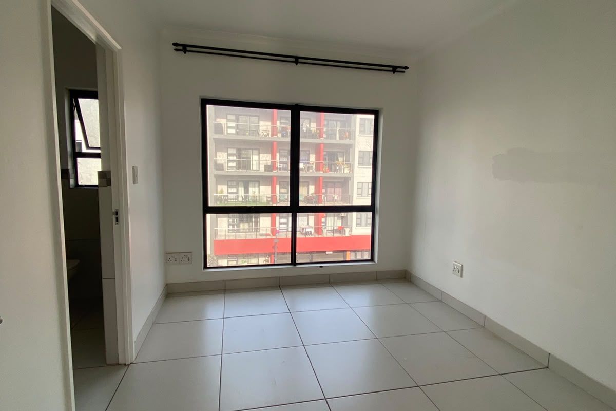 An empty bedroom featuring neutral tiled flooring, a large window with a curtain rod, and access to an adjacent bathroom.