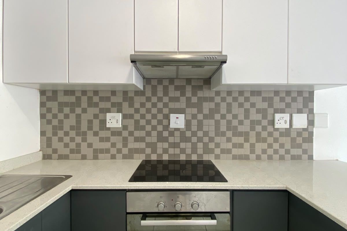 Modern kitchen featuring sleek dark lower cabinetry, white upper cabinets, stone countertops, and a mosaic tile backsplash with integrated appliances.