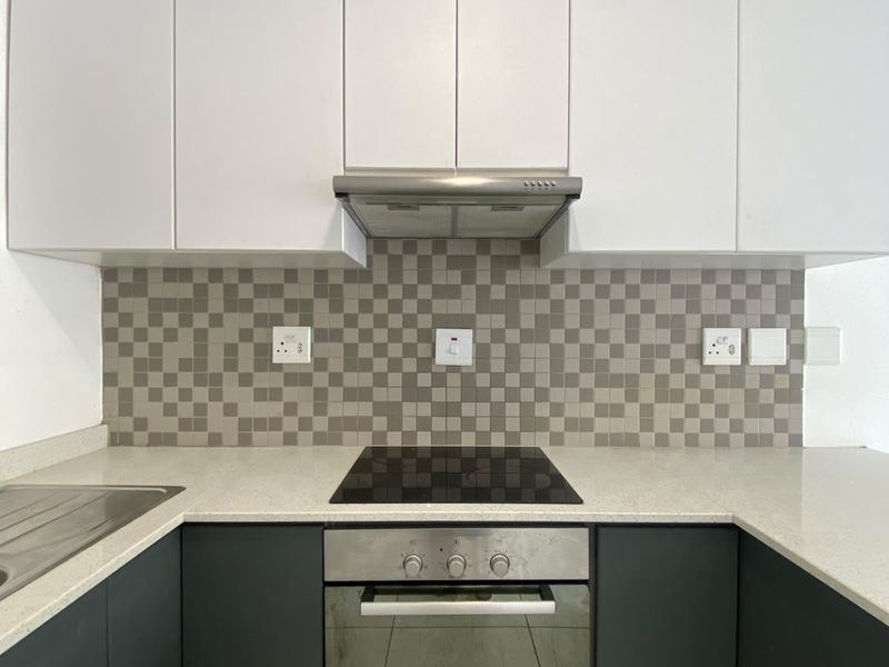 Modern kitchen featuring sleek dark lower cabinetry, white upper cabinets, stone countertops, and a mosaic tile backsplash with integrated appliances.