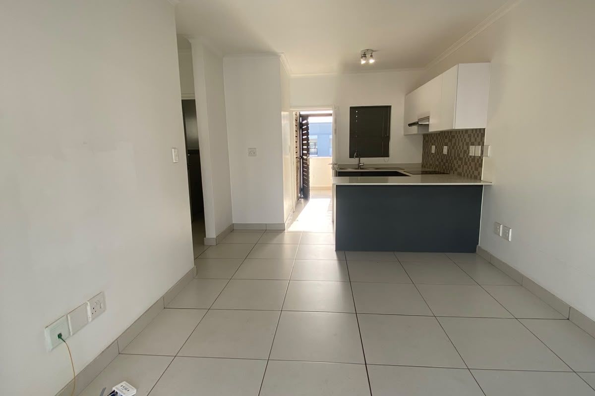 An open-plan living and kitchen area featuring neutral tiled flooring, modern cabinetry, and a breakfast island, leading to an outdoor balcony.