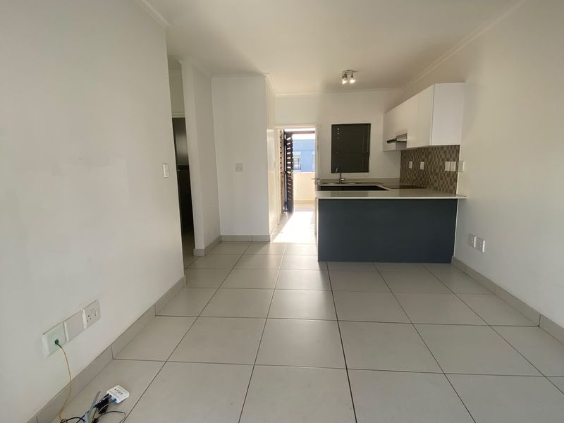 An open-plan living and kitchen area featuring neutral tiled flooring, modern cabinetry, and a breakfast island, leading to an outdoor balcony.