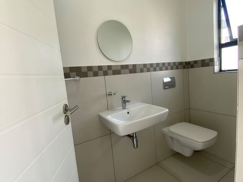 A clean, modern bathroom featuring a wall-mounted basin, wall-mounted toilet, and neutral tiled finishes with a decorative mosaic border.
