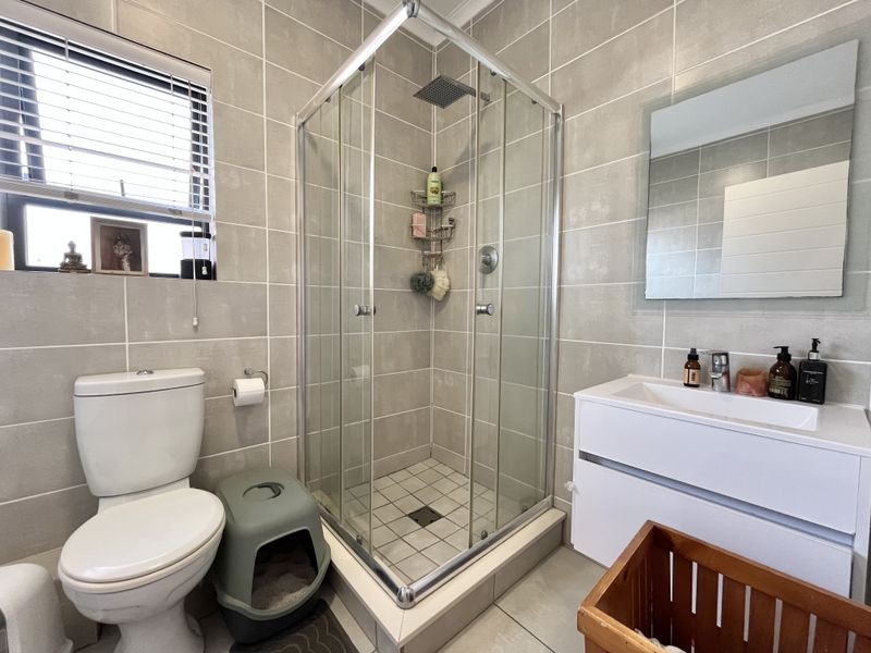 A modern bathroom featuring a glass-enclosed shower, a sleek vanity unit, and neutral wall tiling.