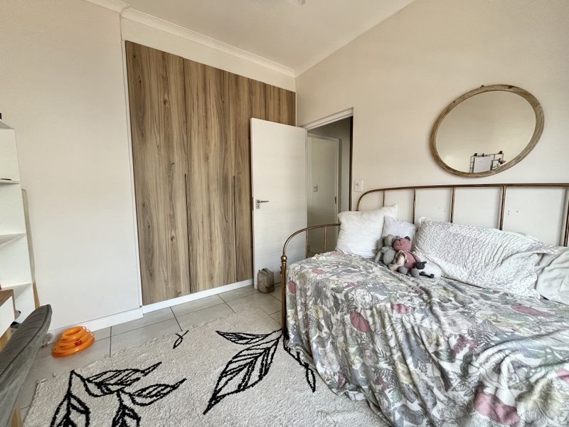 A well-maintained bedroom featuring modern wood-finish built-in cupboards and neutral tiled flooring.