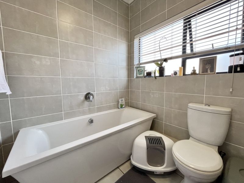 A clean, modern bathroom featuring neutral wall tiling, a built-in bathtub with wall-mounted fixtures, and a standard toilet.