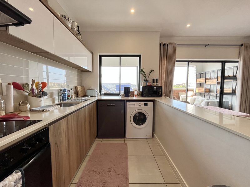 Modern open-plan kitchen featuring sleek cabinetry, stone countertops, and integrated appliances, seamlessly flowing into the living area with access to a balcony.