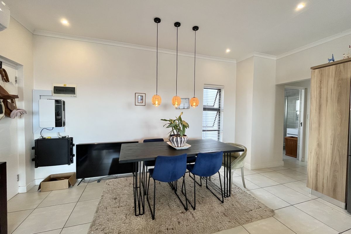 An open-plan dining area featuring tiled flooring, modern pendant lighting, and neutral walls, with a view into the adjacent bathroom.