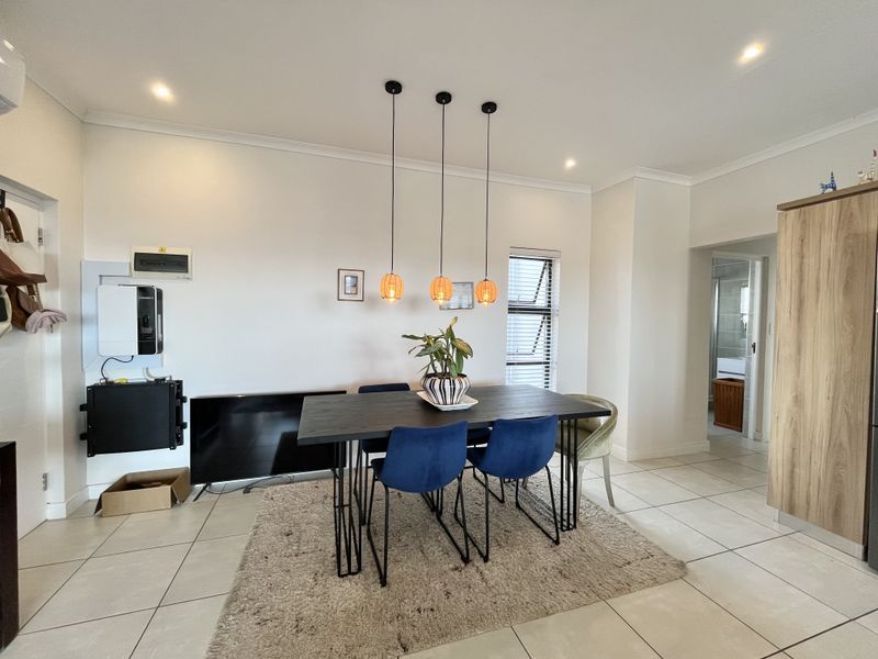 An open-plan dining area featuring tiled flooring, modern pendant lighting, and neutral walls, with a view into the adjacent bathroom.