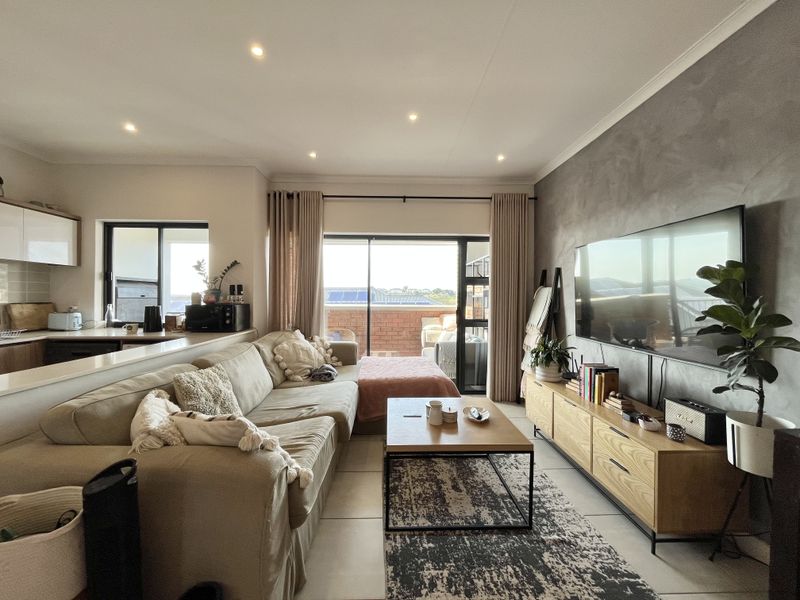An open-plan living area featuring a modern kitchen, tiled floors, a textured feature wall, and direct access to a private balcony through sliding glass doors.