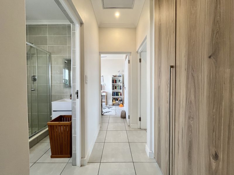 A bright hallway featuring tiled flooring, built-in wooden cupboards, and direct access to an adjacent bathroom and bedroom.