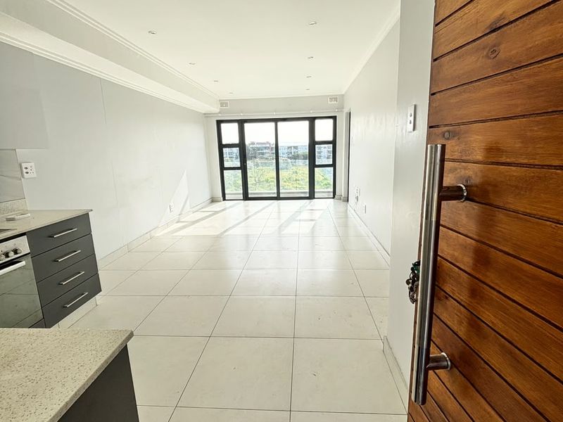 Bright open-plan living area featuring tiled floors, a modern kitchen with built-in appliances, and large sliding doors leading to an outdoor space.