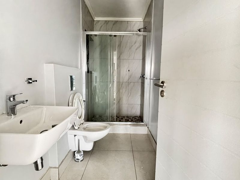 A clean, modern bathroom featuring a wall-mounted basin, wall-hung toilet, and a glass-enclosed shower with neutral tiling.