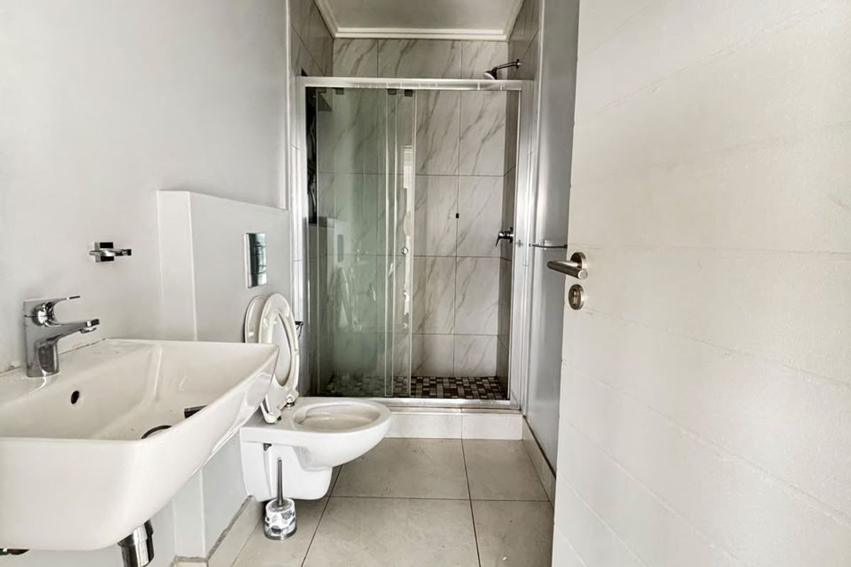 A clean, modern bathroom featuring a wall-mounted basin, wall-hung toilet, and a glass-enclosed shower with neutral tiling.