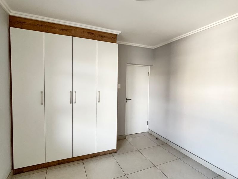 A clean, empty bedroom featuring neutral tiled flooring and modern white built-in cupboards with wood-look trim.