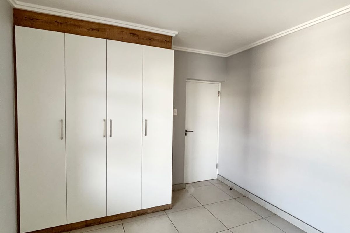 A clean, empty bedroom featuring neutral tiled flooring and modern white built-in cupboards with wood-look trim.