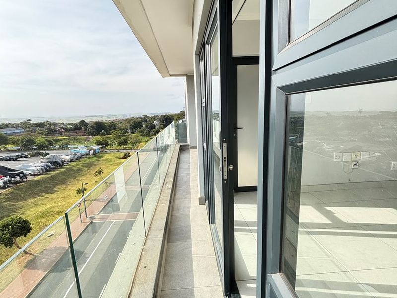 A modern, spacious balcony featuring a sleek glass balustrade, tiled flooring, and large sliding doors providing seamless access to the interior living space.