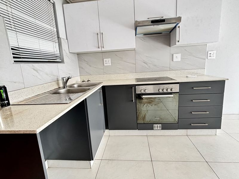 Modern kitchen featuring two-tone cabinetry, stone countertops, integrated electric hob, oven, extractor fan, and tiled flooring.