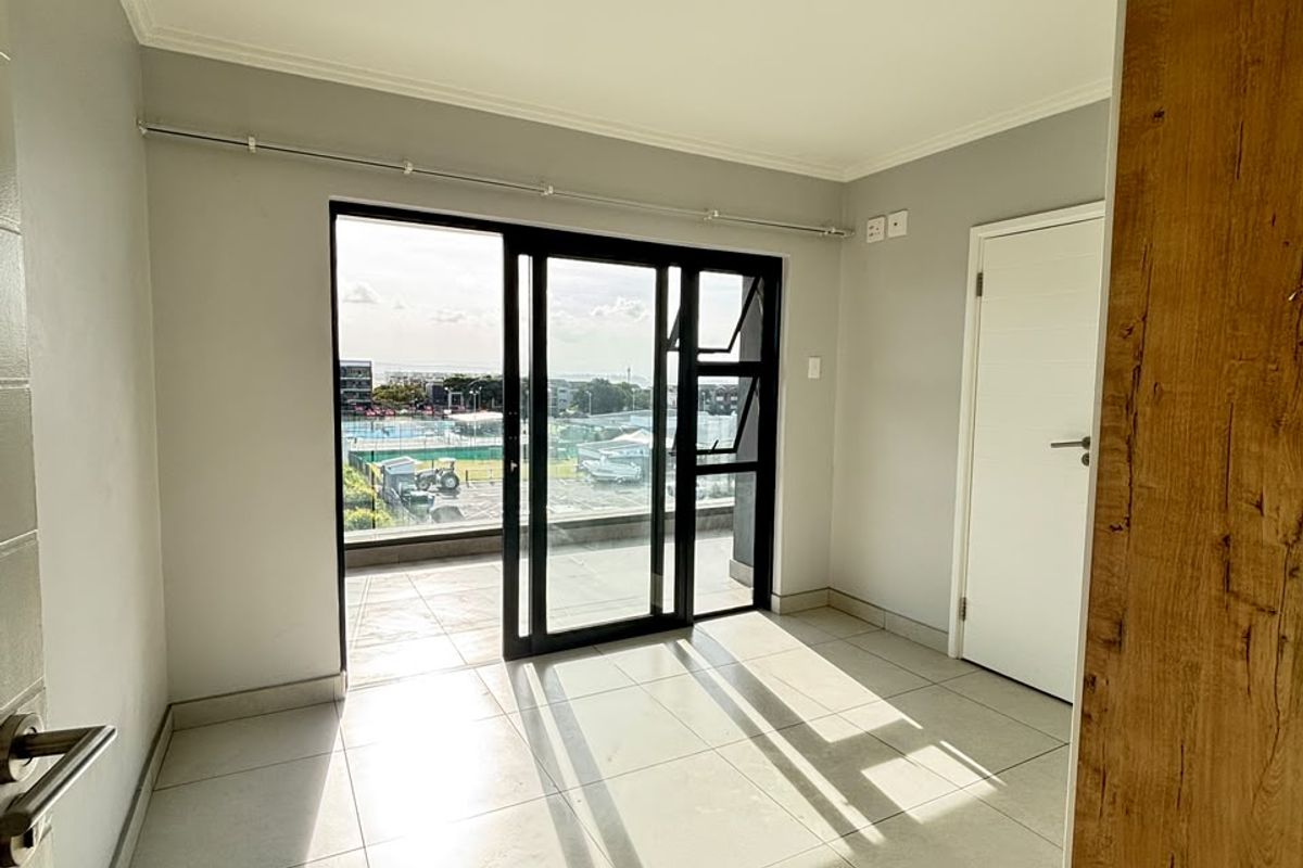 An empty, well-lit living area featuring large sliding glass doors that open onto a balcony, with neutral tiled flooring and modern finishes.