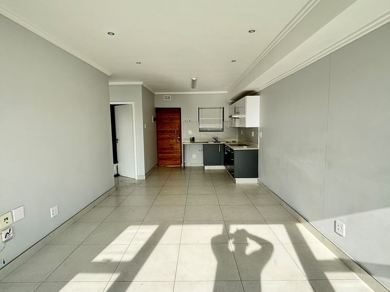 An open-plan living and kitchen area featuring neutral tiled flooring, recessed lighting, and modern kitchen cabinetry with a functional layout.