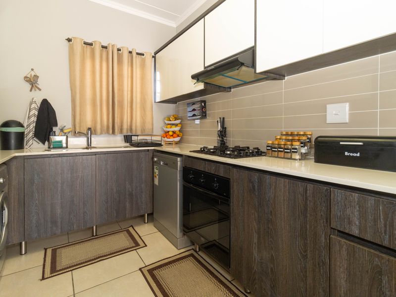 Modern kitchen featuring dark wood-grain cabinetry, stone countertops, a gas hob, built-in oven, extractor fan, and a tiled backsplash.