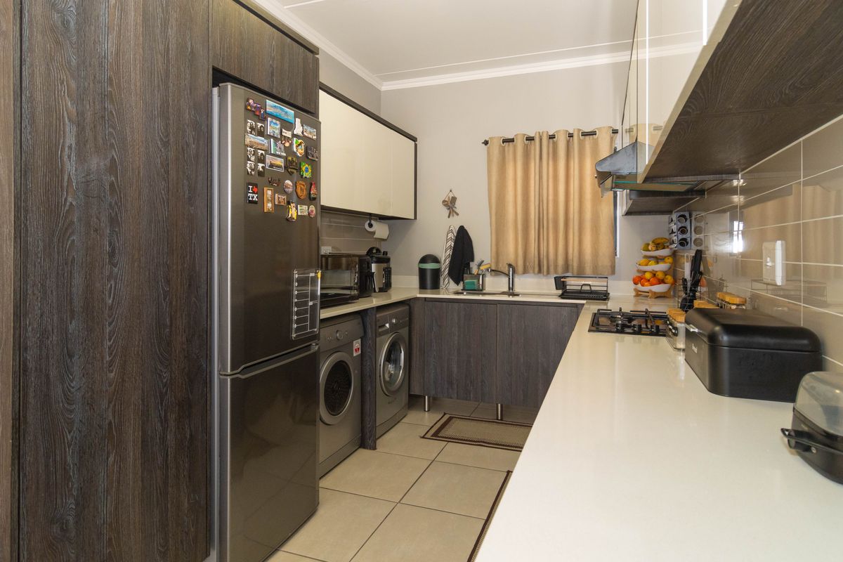 Modern kitchen featuring dark wood-grain cabinetry, stone countertops, integrated gas hob, extractor fan, and tiled flooring with space for laundry appliances.