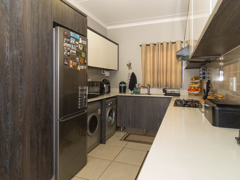 Modern kitchen featuring dark wood-grain cabinetry, stone countertops, integrated gas hob, extractor fan, and tiled flooring with space for laundry appliances.