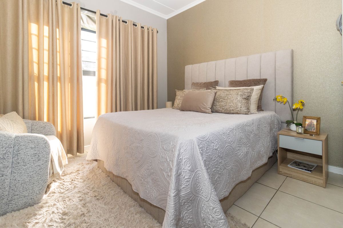 A well-maintained bedroom featuring tiled flooring, neutral tones, and an accent wall, providing a comfortable and inviting living space.
