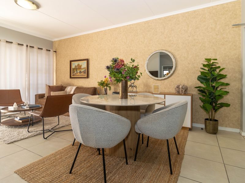 An open-plan living and dining area featuring tiled flooring, neutral textured wallpaper, and a sliding glass door providing access to the exterior.