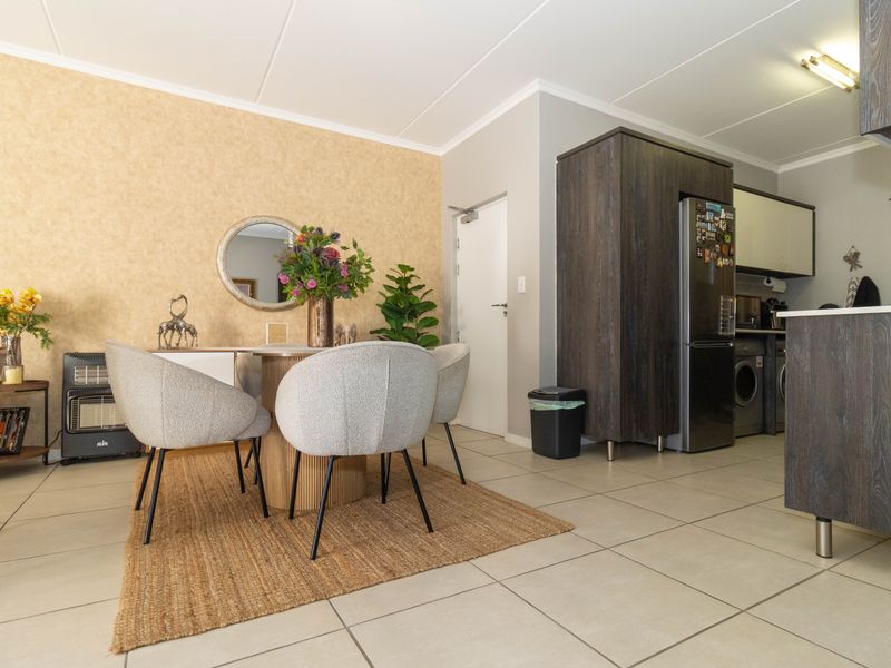 Open-plan living and dining area featuring tiled flooring, neutral wall finishes, and a functional kitchen space with built-in cabinetry and integrated laundry appliances.