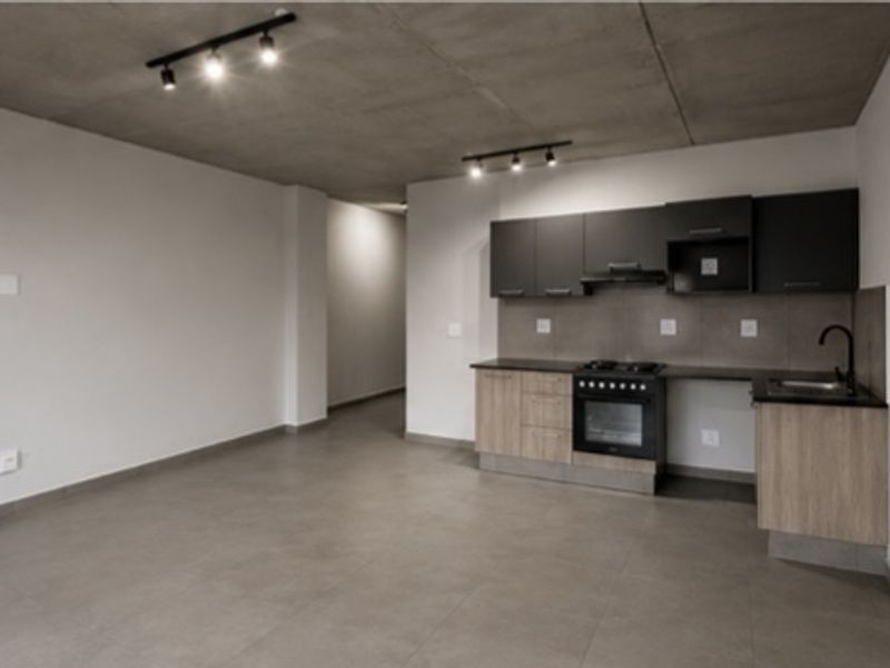 Modern open-plan living area featuring an exposed concrete ceiling, track lighting, and a contemporary kitchen with built-in cabinetry, gas hob, and oven.