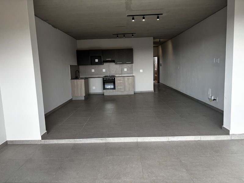 Spacious open-plan living and kitchen area featuring modern cabinetry, built-in oven, hob, and large format floor tiles throughout.