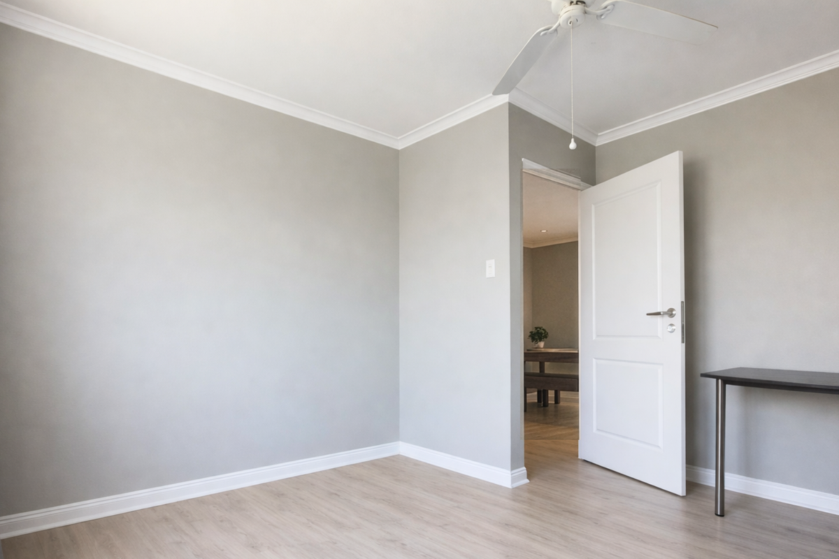 A bright, empty bedroom featuring neutral grey walls, light laminate flooring, and a ceiling fan, offering a clean and versatile living space.