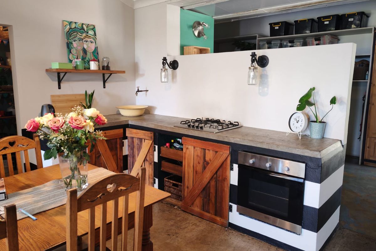 A rustic-style kitchen featuring a concrete countertop, built-in gas hob, oven, and custom wooden cabinetry with a unique black and white striped base.