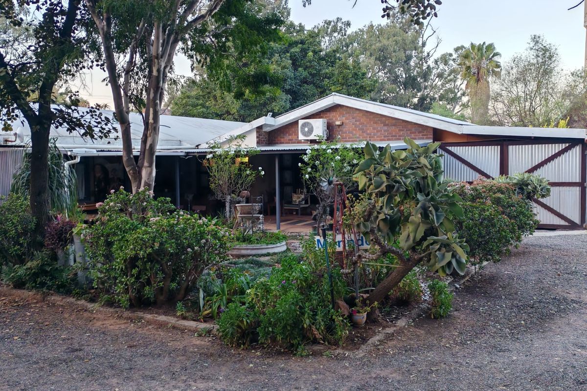 Rear view of a brick house featuring a covered patio area, corrugated metal roofing, and established garden surroundings.