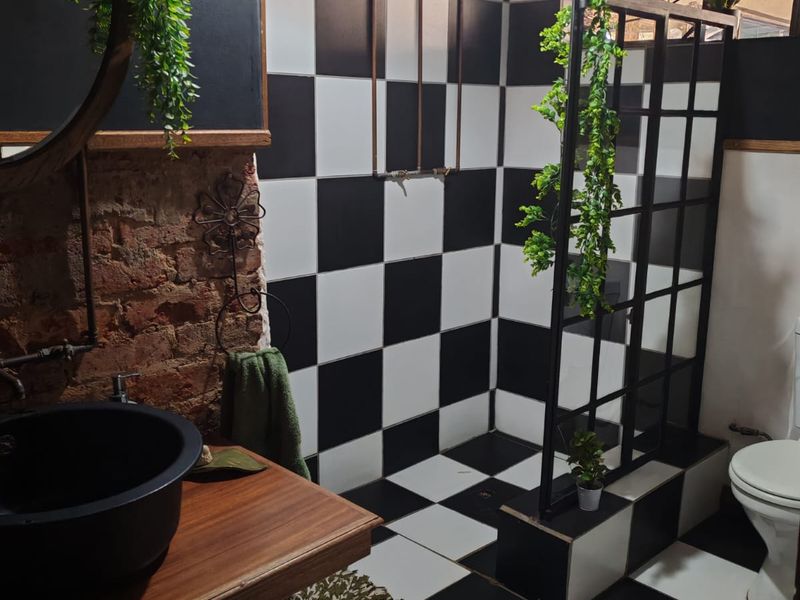 A stylish bathroom featuring a bold black and white checkerboard tile design, exposed brick wall, walk-in shower with black frame, and a unique vessel sink.