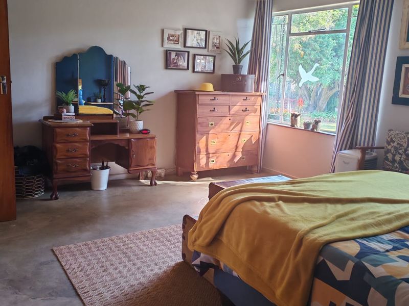 A spacious bedroom featuring a unique pressed metal ceiling, polished concrete flooring, and a large window providing natural light and garden views.