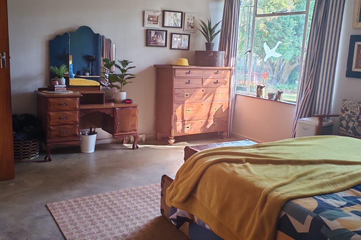 A spacious bedroom featuring a unique pressed metal ceiling, polished concrete flooring, and a large window providing natural light and garden views.