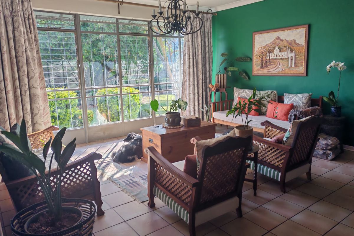 A bright living room featuring large steel-framed windows with security bars, tiled flooring, and a decorative wrought iron chandelier.