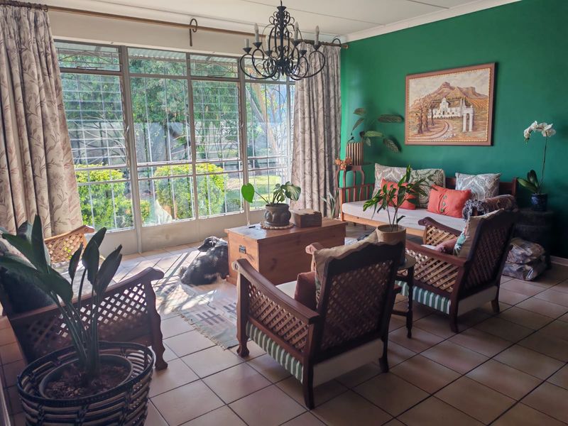 A bright living room featuring large steel-framed windows with security bars, tiled flooring, and a decorative wrought iron chandelier.