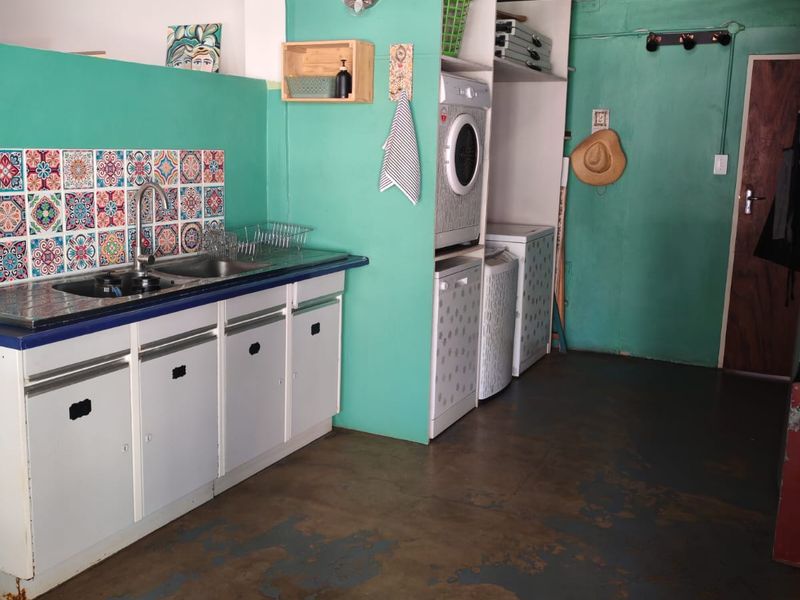 Functional laundry area featuring built-in cabinetry, a stainless steel sink, decorative tiled backsplash, and dedicated space for laundry appliances.