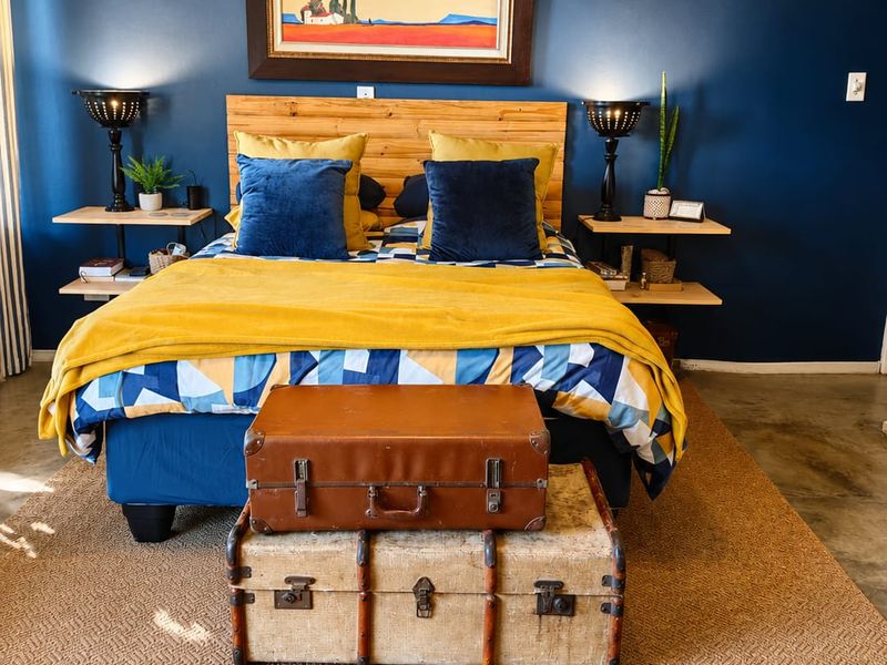 A well-maintained bedroom featuring a polished concrete floor, a custom timber headboard, and floating bedside shelves against a bold navy accent wall.